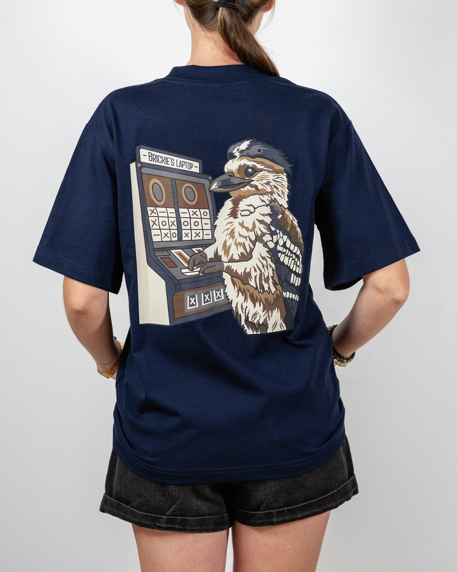 Navy t-shirt with a graphic of a bird and slot machine on the back, worn by a person and with the words "Brickie's Laptop".