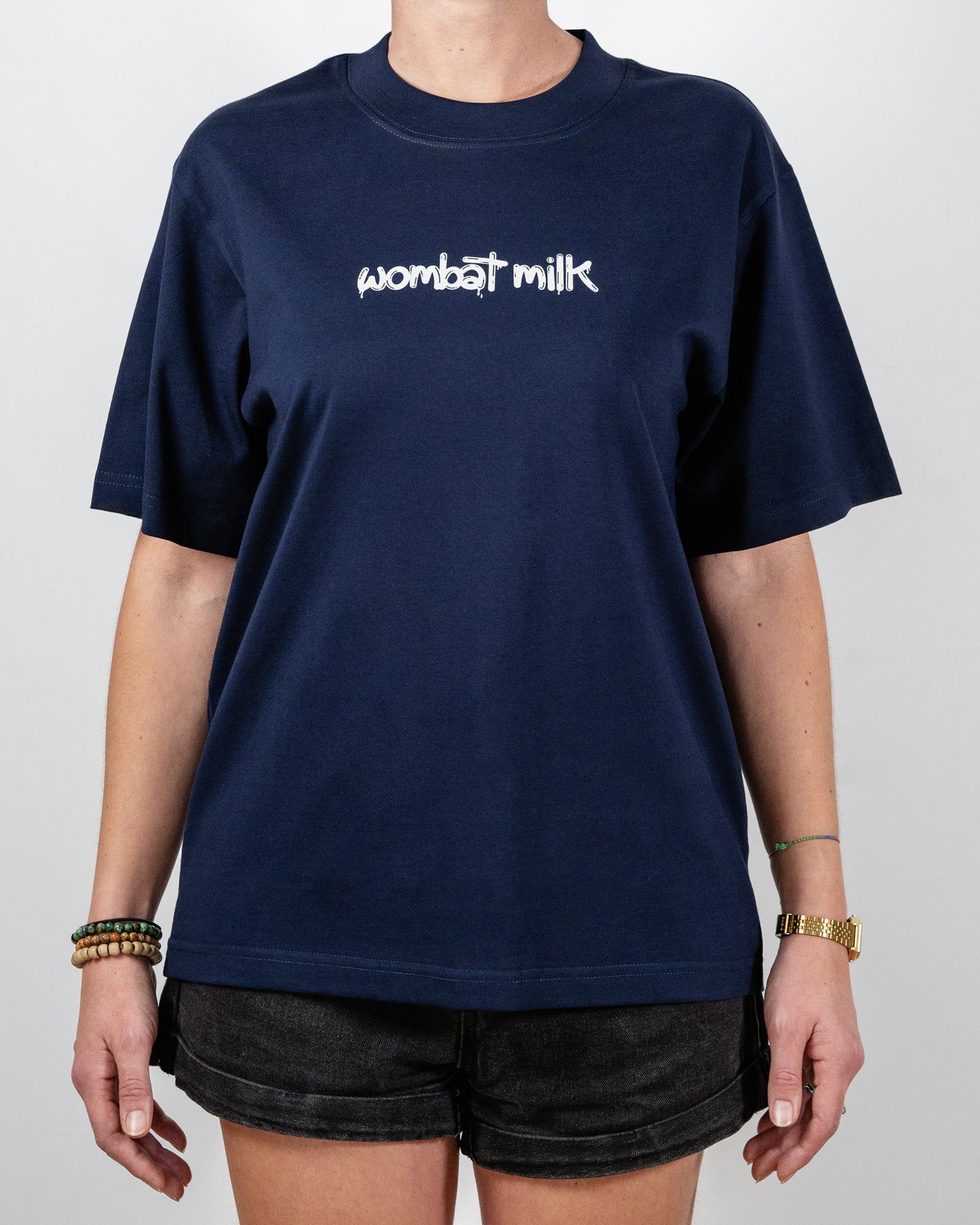 Person wearing a navy blue t-shirt with 'wombat milk' text standing against a plain background.