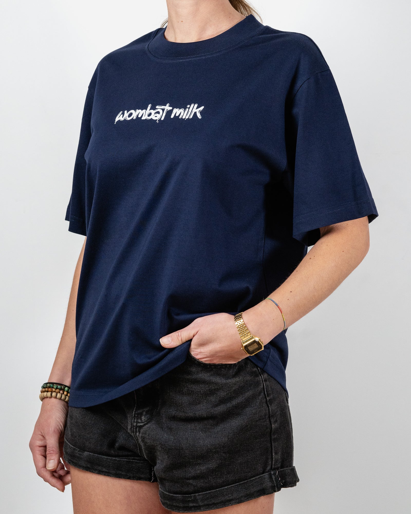 Person wearing a navy blue t-shirt with 'wombat milk' text standing against a plain background.