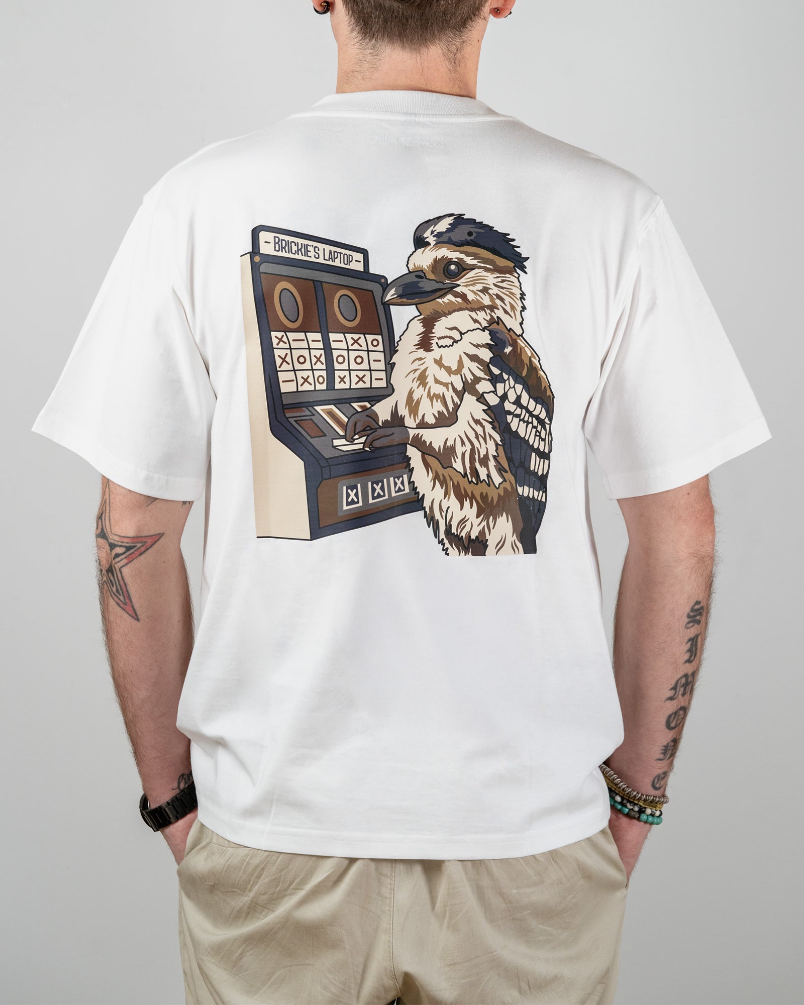 White t-shirt with a graphic of a bird and slot machine on the back, worn by a person and with the words "Brickie's Laptop".