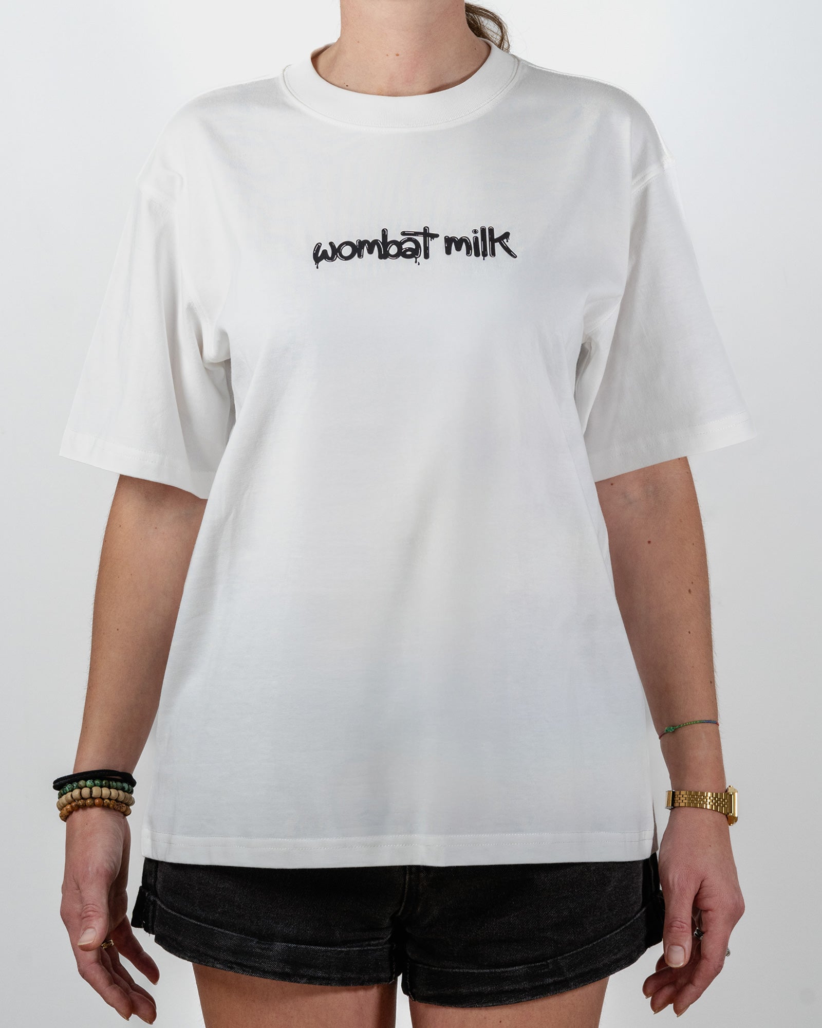Person wearing a white t-shirt with 'wombat milk' text standing against a plain background.