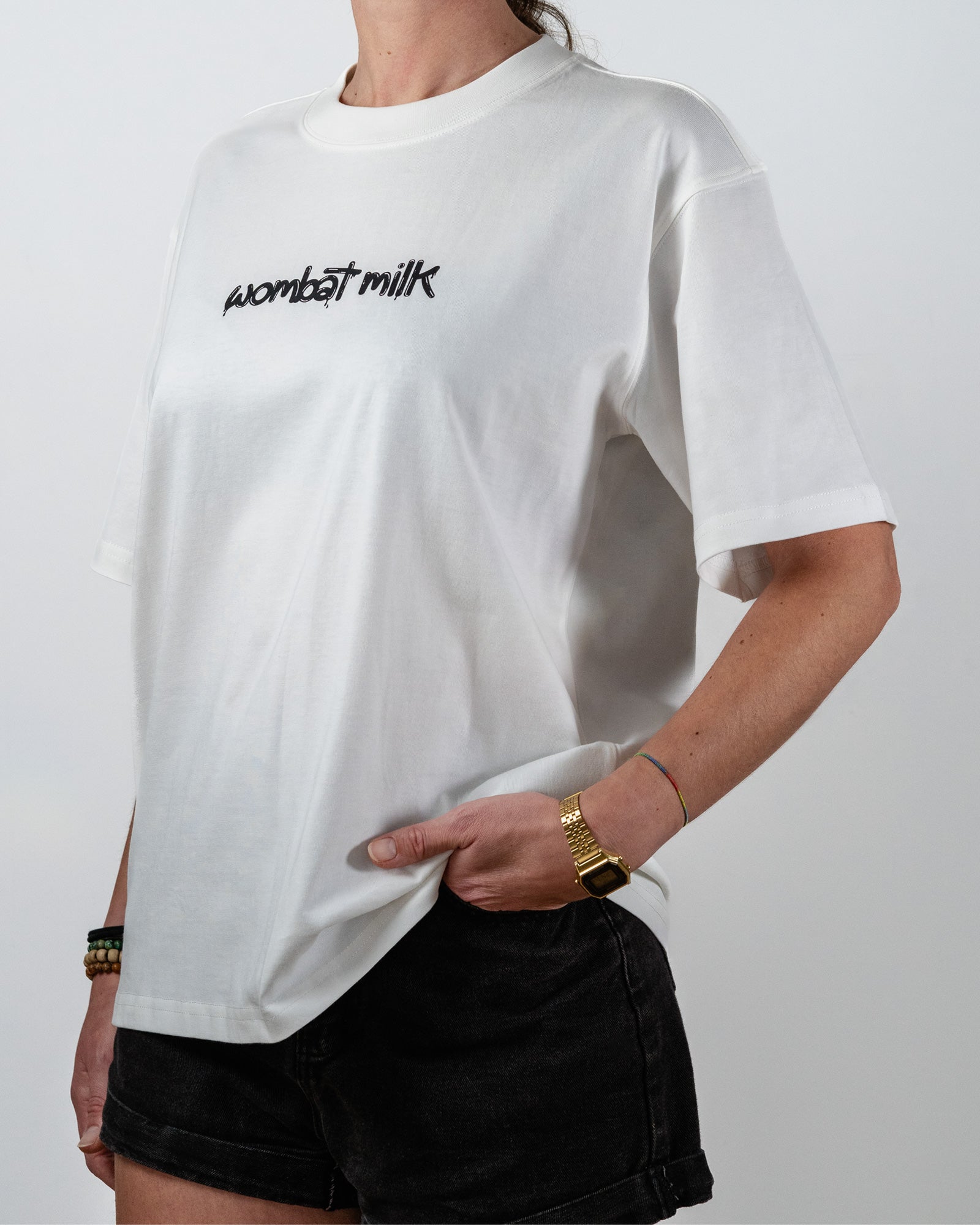 Person wearing a white t-shirt with 'wombat milk' black text standing against a plain background.