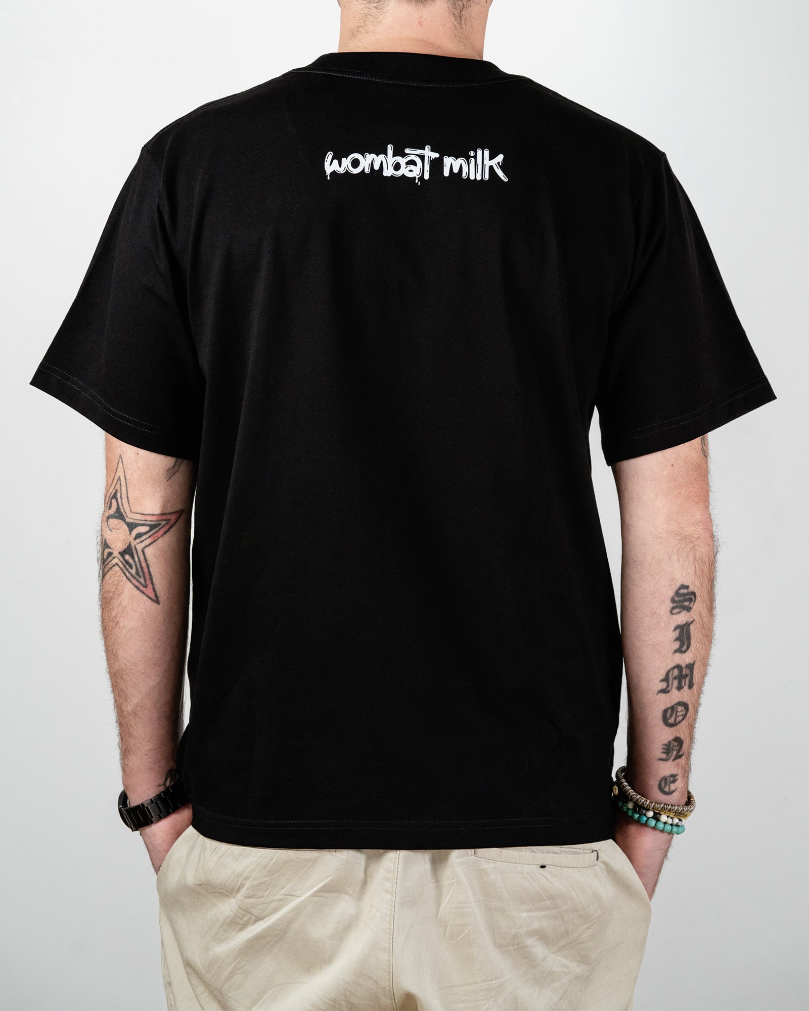 Person wearing a black t-shirt with 'wombat milk' text on the back, standing against a plain background.