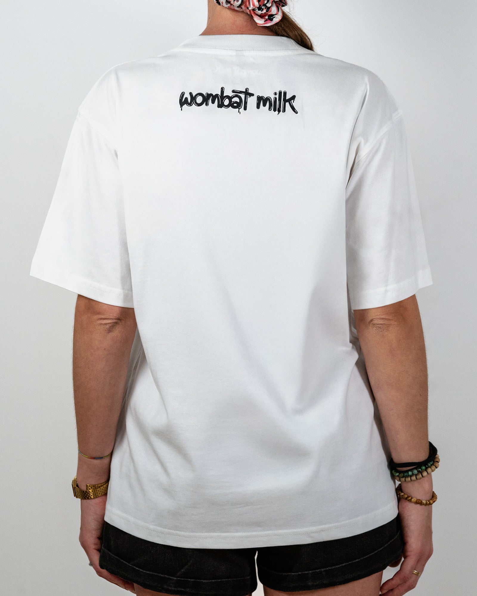 Person wearing a white t-shirt with 'wombat milk' text on the back against a plain background.