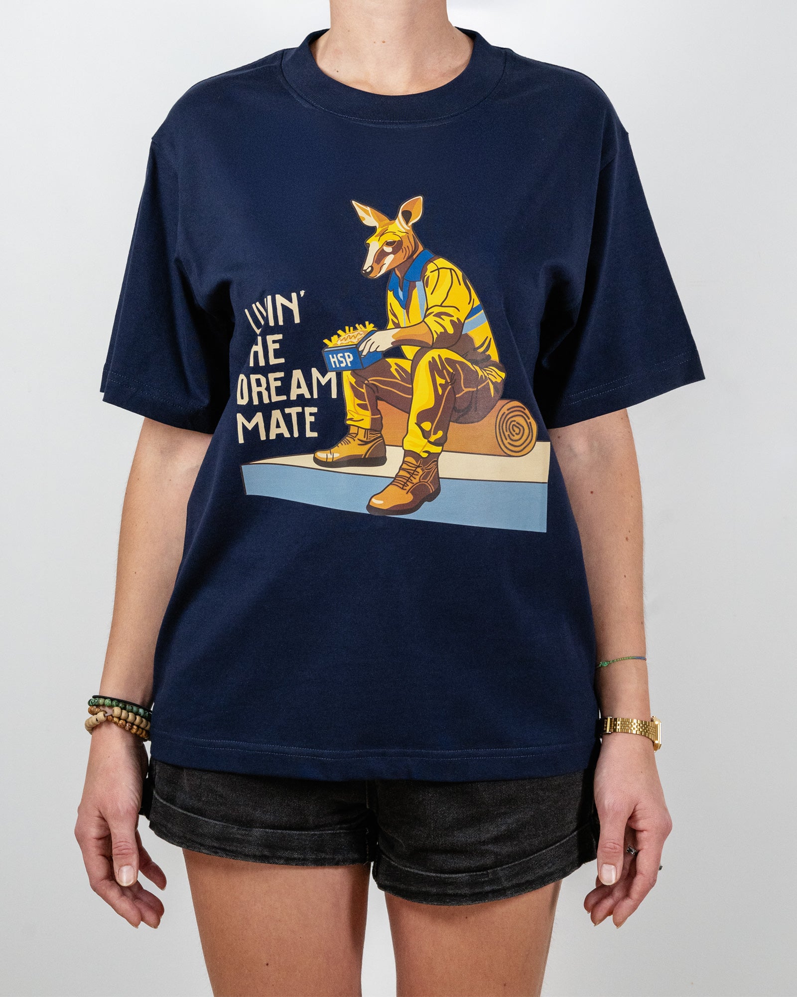 Navy blue t-shirt with a "Livin' The Dream Mate" graphic —featuring a kangaroo wearing a hi-vis set of overalls and work boots, eating an HSP kebab pack whilst sitting on a wooden log that is on top of a concrete slab.