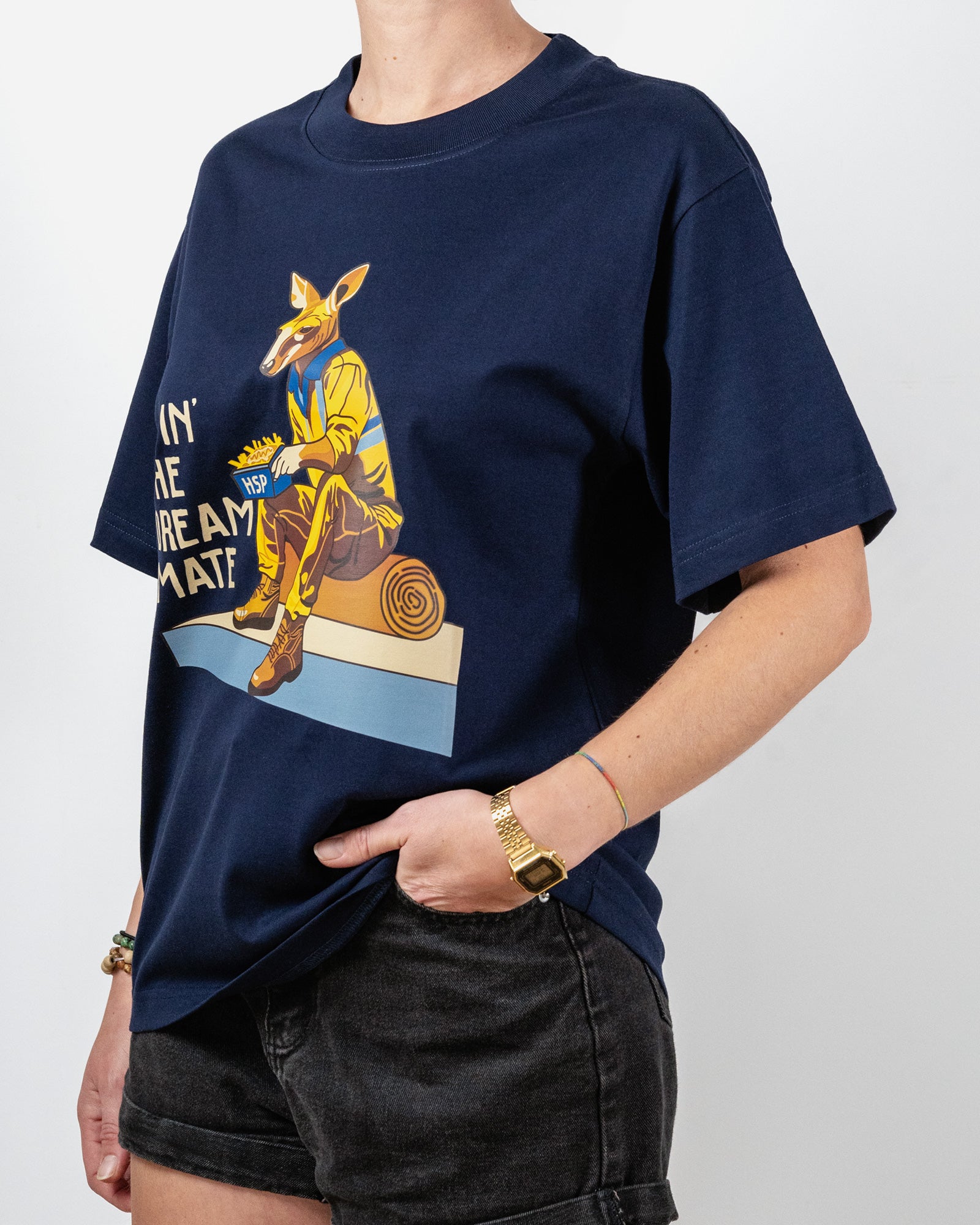 Navy blue t-shirt with a "Livin' The Dream Mate" graphic —featuring a kangaroo wearing a hi-vis set of overalls and work boots, eating an HSP kebab pack whilst sitting on a wooden log that is on top of a concrete slab.