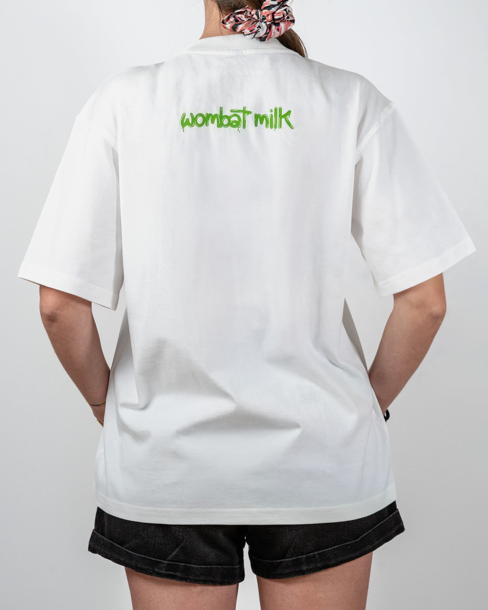 Person wearing a white shirt with 'wombat milk' text on the back against a plain background