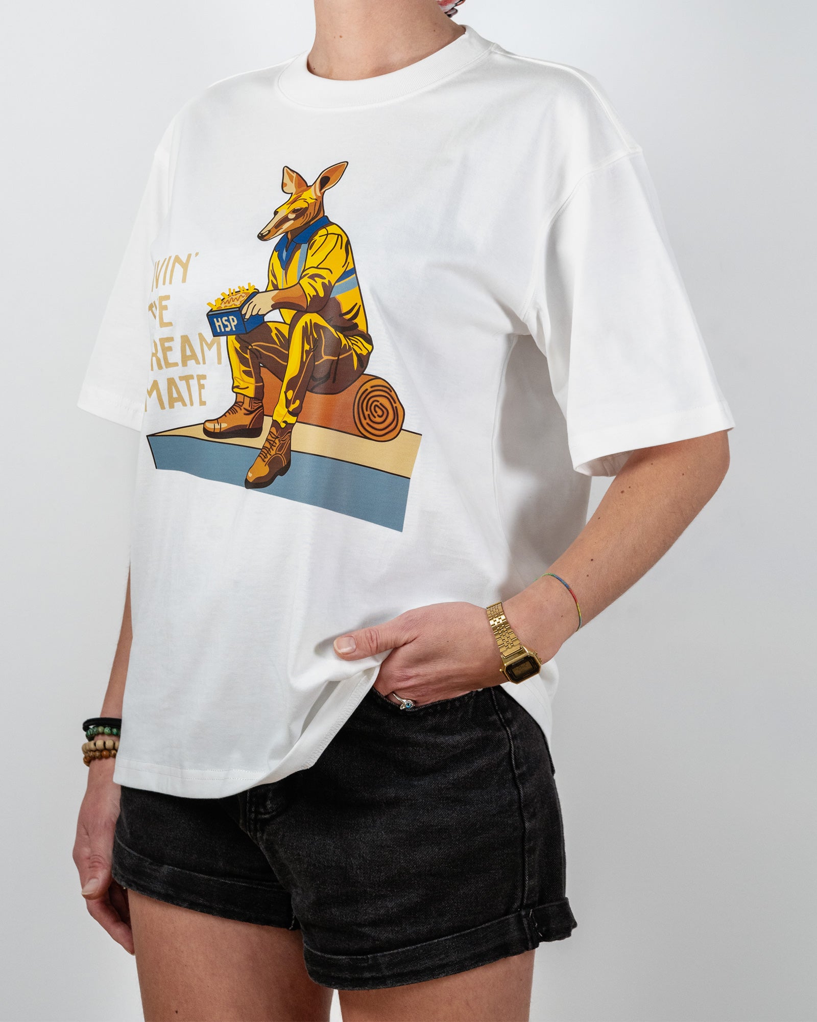 White t-shirt with a graphic design of a kangaroo wearing boots and a hat, sitting on a wooden log with the wording "livin' the dream mate" - photo taken on the side.