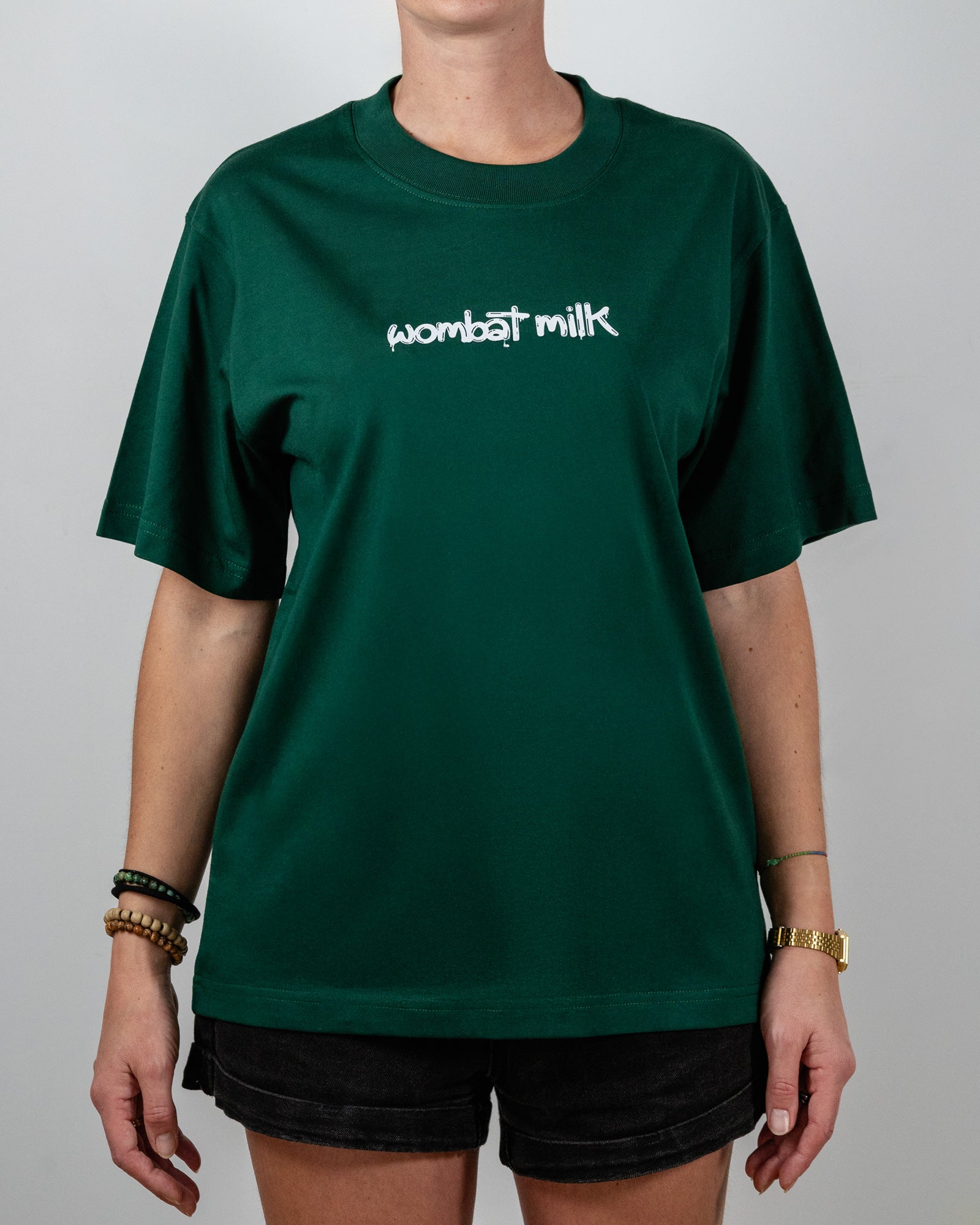 Person wearing a green t-shirt with 'wombat milk' text standing against a plain background.