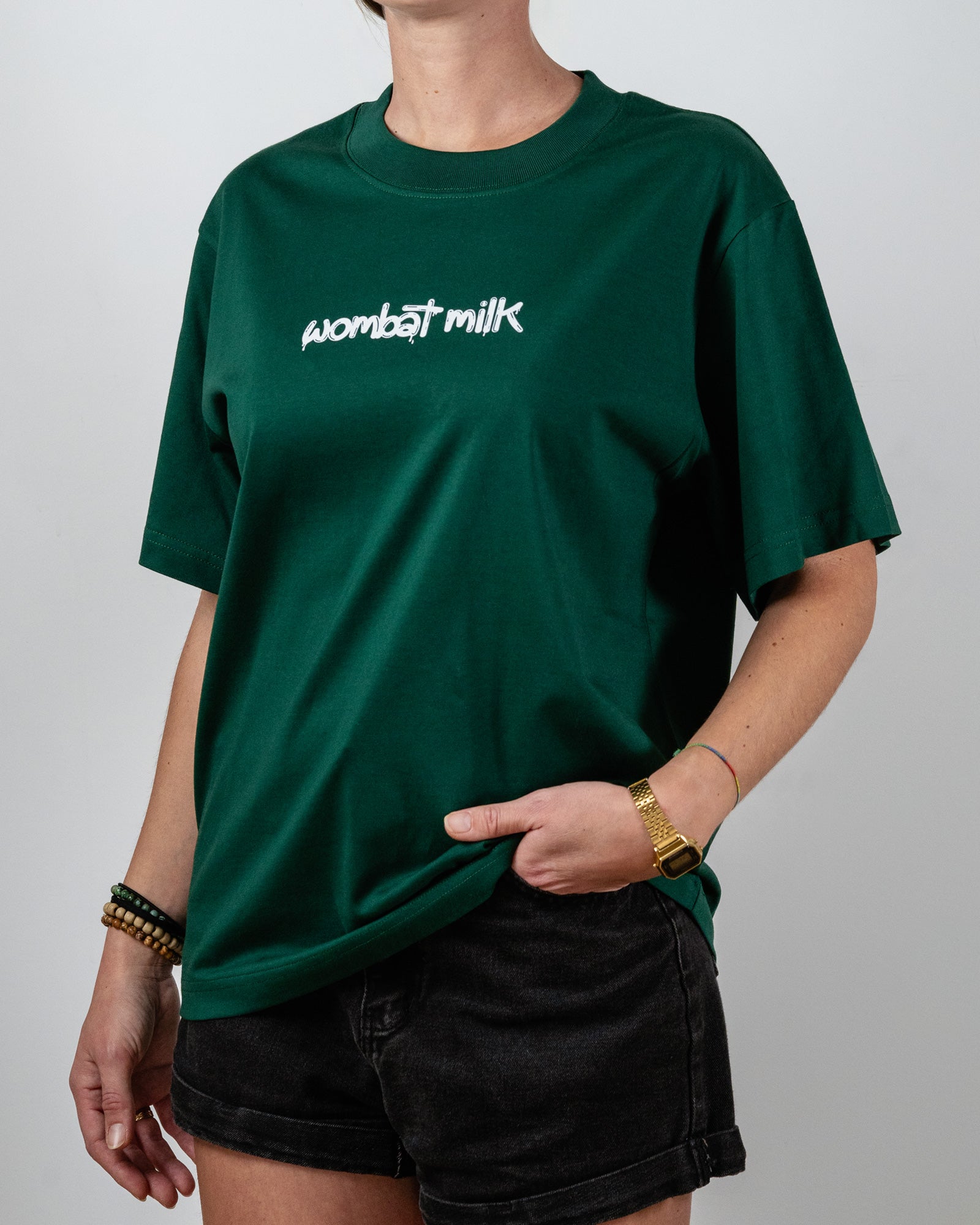 Person wearing a green t-shirt with 'wombat milk' text standing against a plain background.