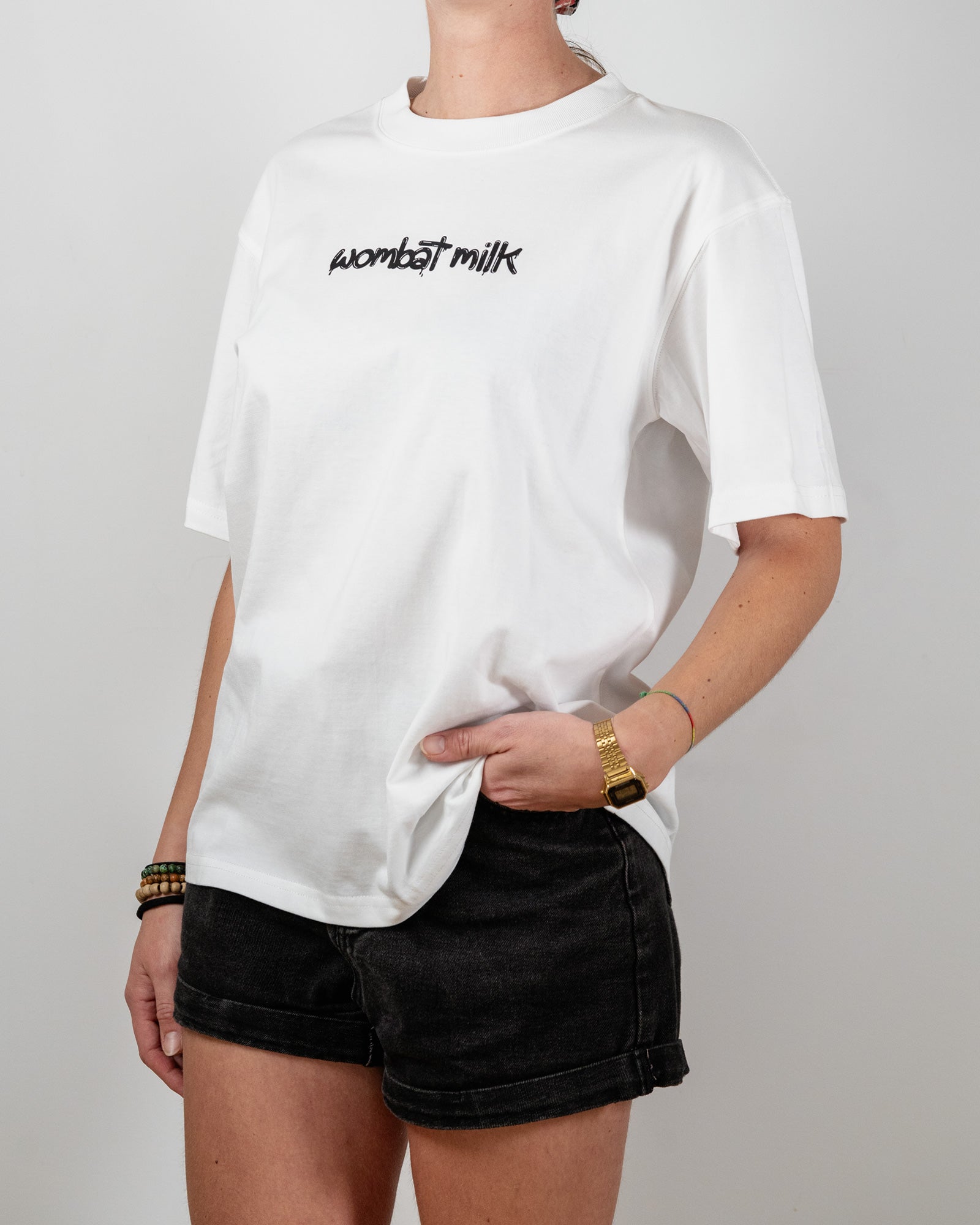 Person wearing a white t-shirt with 'wombat milk' text standing against a plain background.