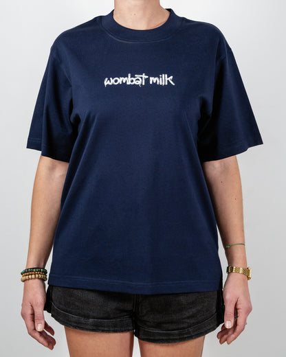 Person wearing a navy blue t-shirt with 'wombat milk' text standing against a plain background.