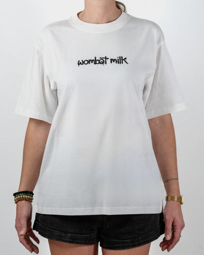Person wearing a white t-shirt with 'wombat milk' text standing against a plain background.