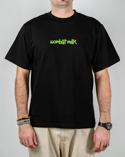 Person wearing a black t-shirt with 'wombat milk' text standing against a plain background.