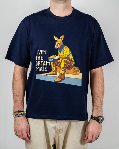 Navy blue t-shirt with a "Livin' The Dream Mate" graphic —featuring a kangaroo wearing a hi-vis set of overalls and work boots, eating an HSP kebab pack whilst sitting on a wooden log that is on top of a concrete slab.