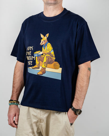 Navy blue t-shirt with a "Livin' The Dream Mate" graphic —featuring a kangaroo wearing a hi-vis set of overalls and work boots, eating an HSP kebab pack whilst sitting on a wooden log that is on top of a concrete slab.