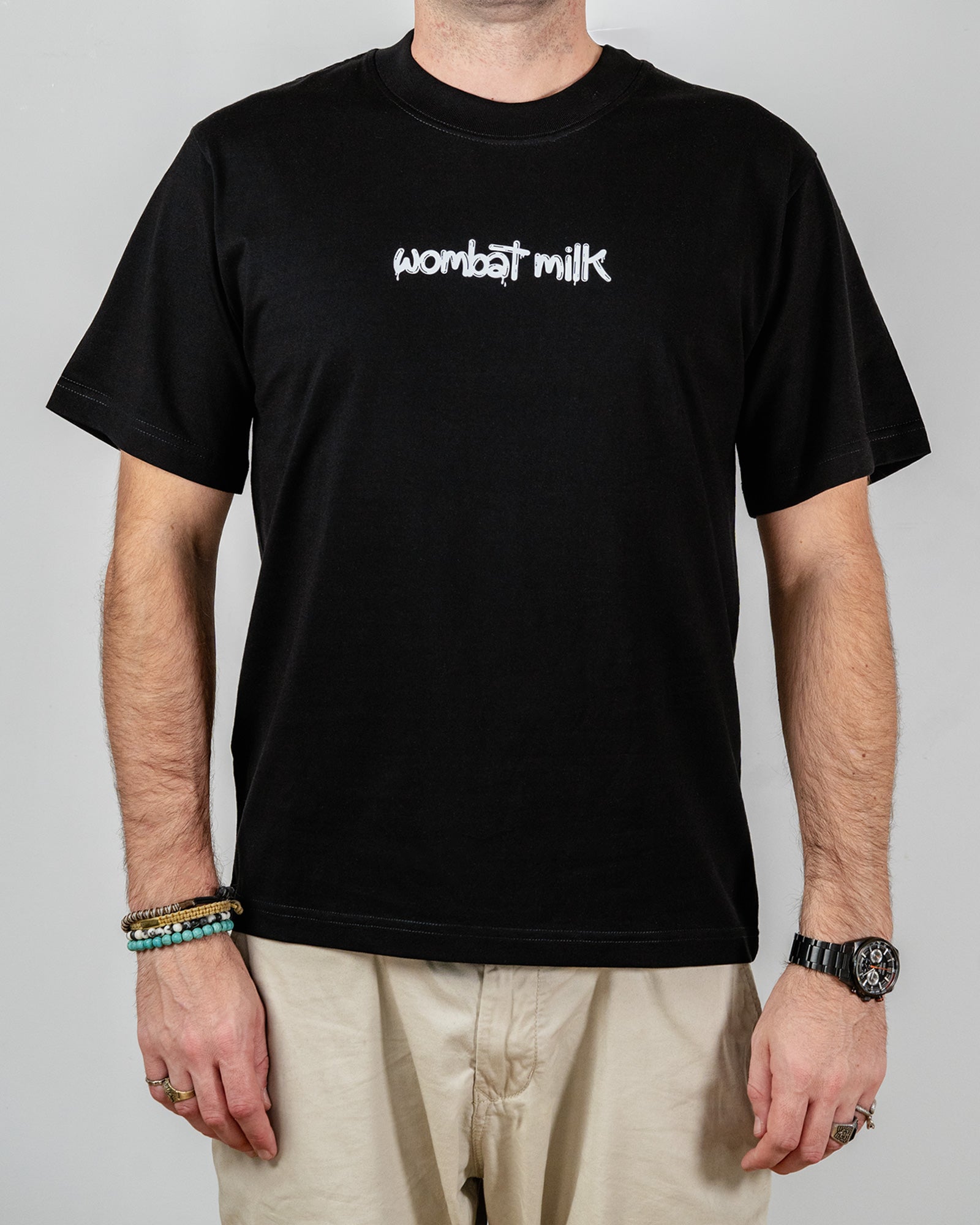Person wearing a black t-shirt with 'Wombat Milk' text standing against a plain background.