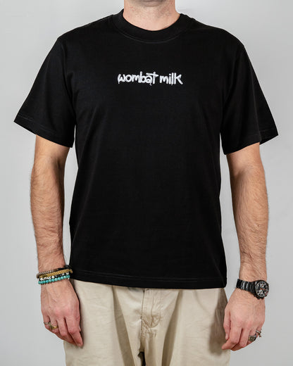 Person wearing a black t-shirt with 'Wombat Milk' text standing against a plain background.
