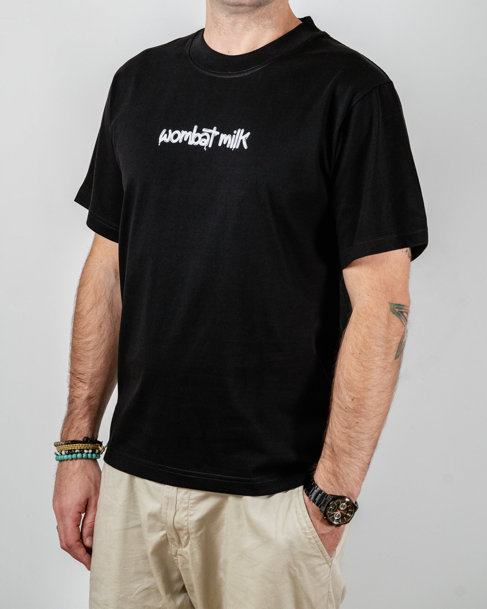 Person wearing a black t-shirt with 'Wombat Milk' text standing against a plain background.