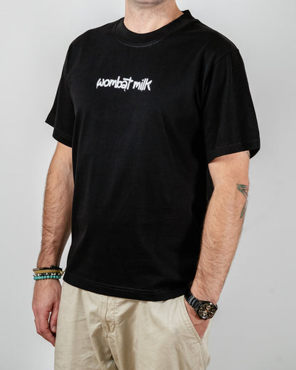 Person wearing a black t-shirt with 'Wombat Milk' text standing against a plain background.