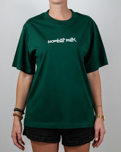 Person wearing a green t-shirt with 'wombat milk' text standing against a plain background.