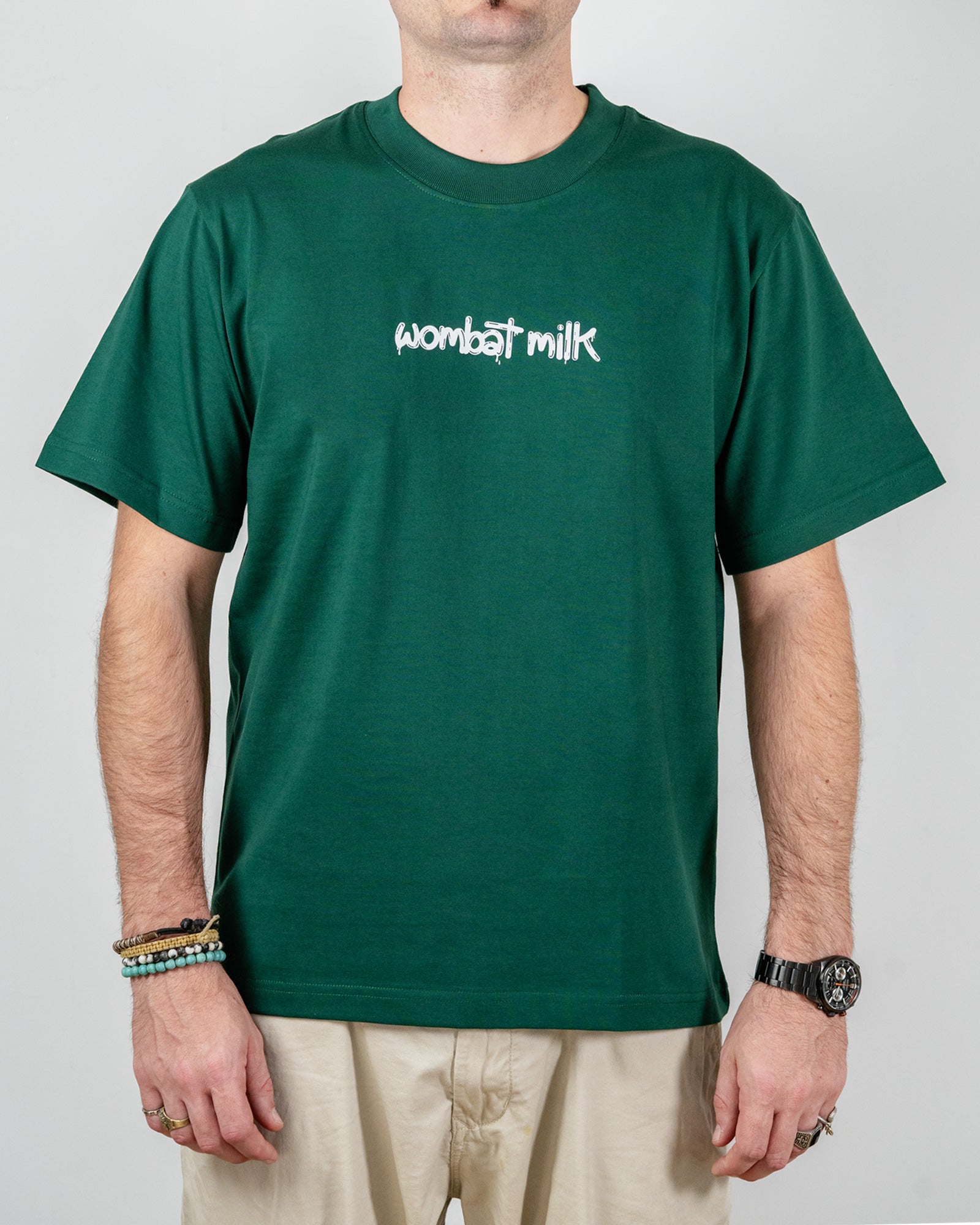 Person wearing a green t-shirt with 'wombat milk' text standing against a plain background.