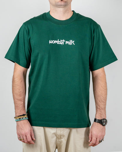 Person wearing a green t-shirt with 'wombat milk' text standing against a plain background.