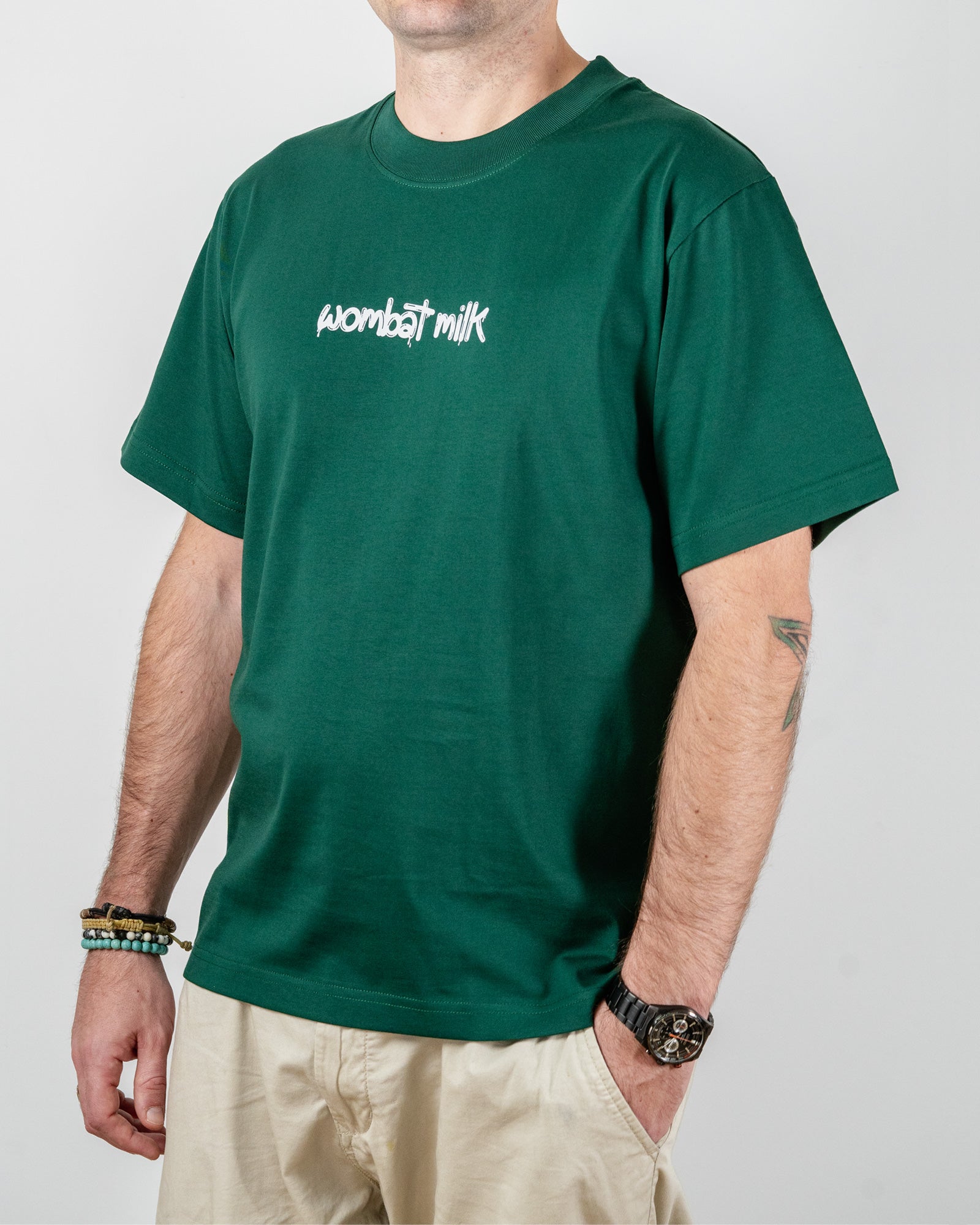 Person wearing a green t-shirt with 'wombat milk' text standing against a plain background.