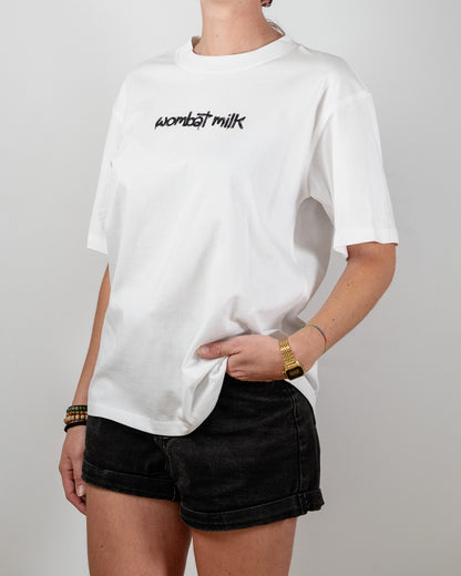 Person wearing a white t-shirt with 'wombat milk' text standing against a plain background.